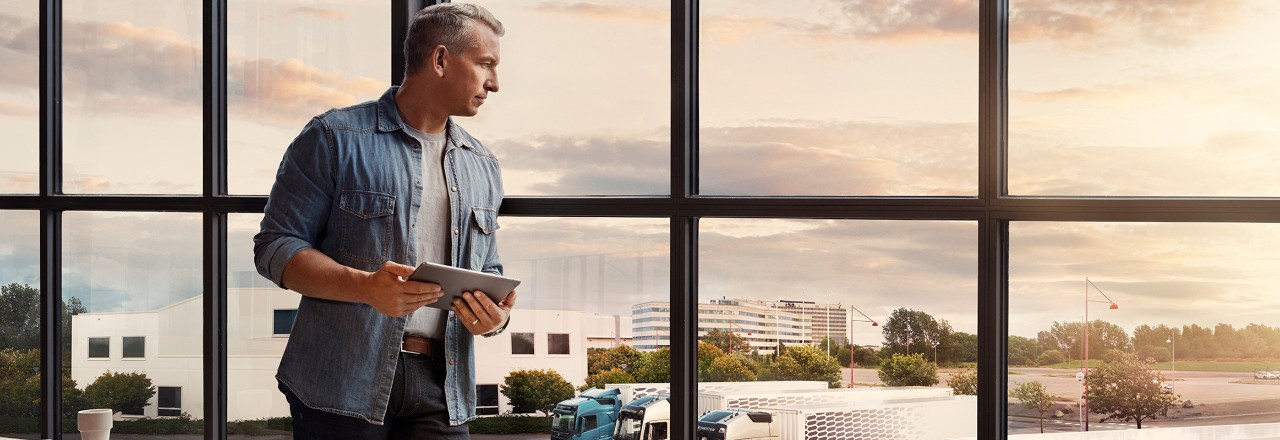 Čovjek koji drži tablet stoji kraj prozora i gleda dolje nad svojim voznim parkom